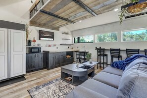 Una cocina moderna con armarios oscuros, un microondas y una mesa de centro. Hay un sofá y una zona de comedor con sillas.