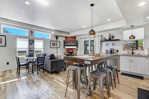 A modern kitchen with a central island, bar stools, a dining area with a sofa, and a TV displaying a welcome message.