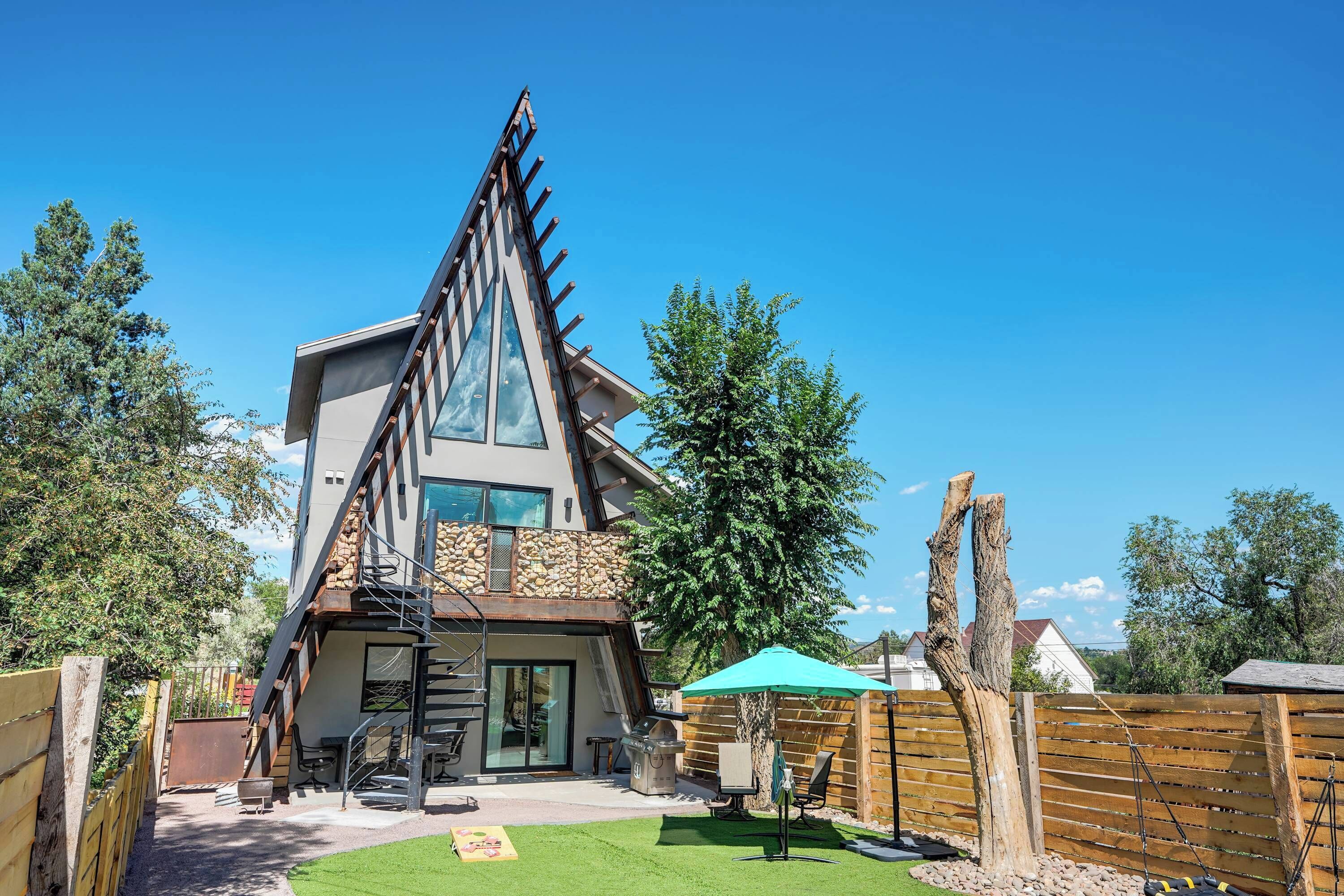 Una casa moderna con un techo triangular distintivo, un patio con mobiliario exterior y una cerca de madera.
