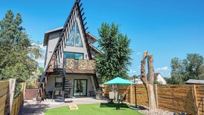 Una casa moderna con un techo triangular distintivo, un patio con mobiliario exterior y una cerca de madera.