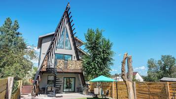 Una casa moderna con un techo triangular distintivo, un patio con mobiliario exterior y una cerca de madera.