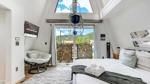 Un dormitorio con cama, una silla, una planta colgante y vistas al exterior.