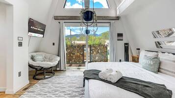 Un dormitorio con cama, una silla, una planta colgante y vistas al exterior.