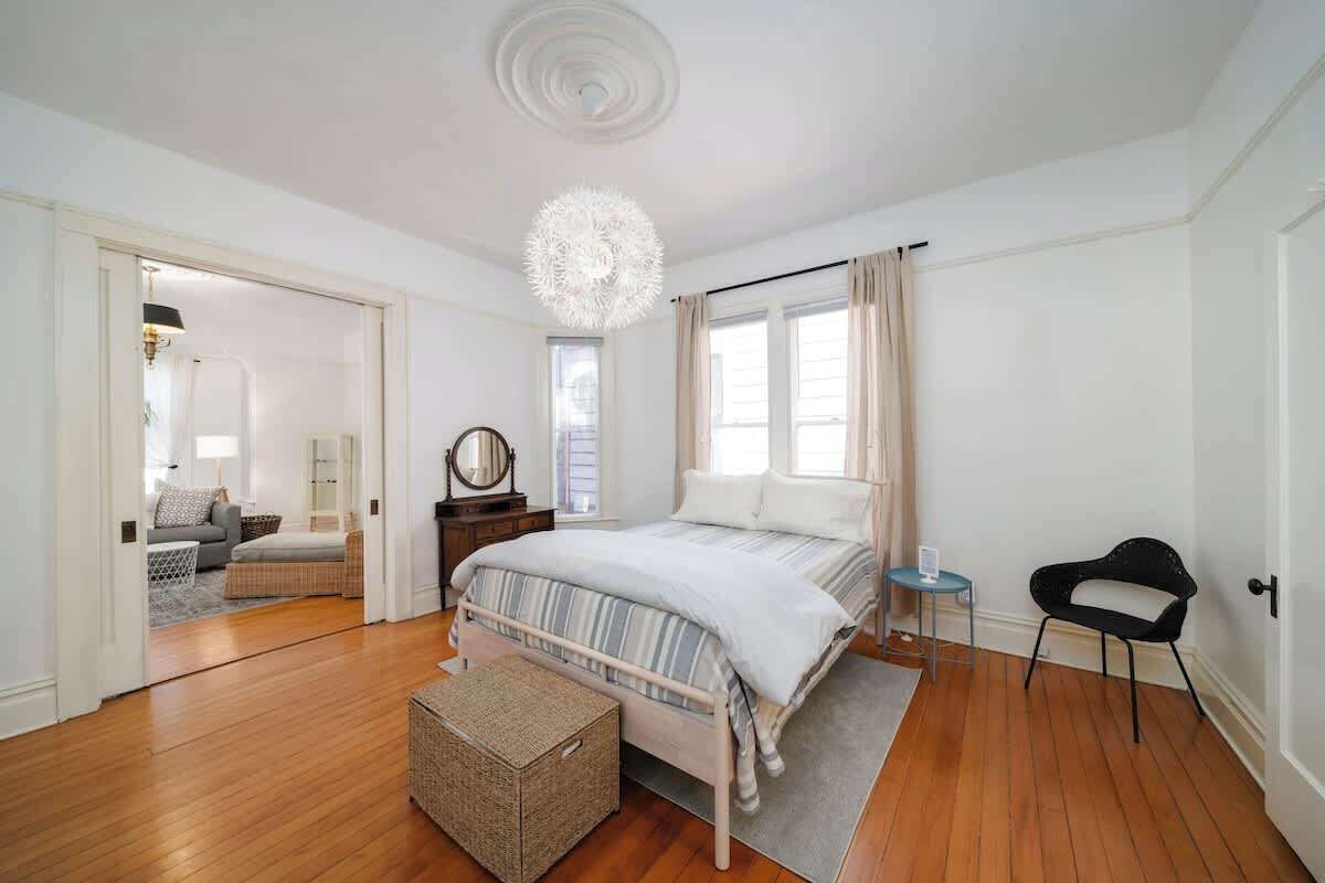 Une chambre à coucher avec un lit, une table de chevet, une chaise, une lampe et une fenêtre.