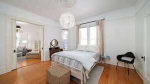 Une chambre à coucher avec un lit, une table de chevet, une chaise, une lampe et une fenêtre.