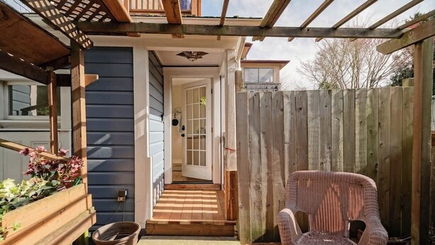 Une terrasse en bois avec une chaise en osier, un jardinier en bois orné de fleurs et une clôture en bois.