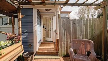 Une terrasse en bois avec une chaise en osier, un jardinier en bois orné de fleurs et une clôture en bois.