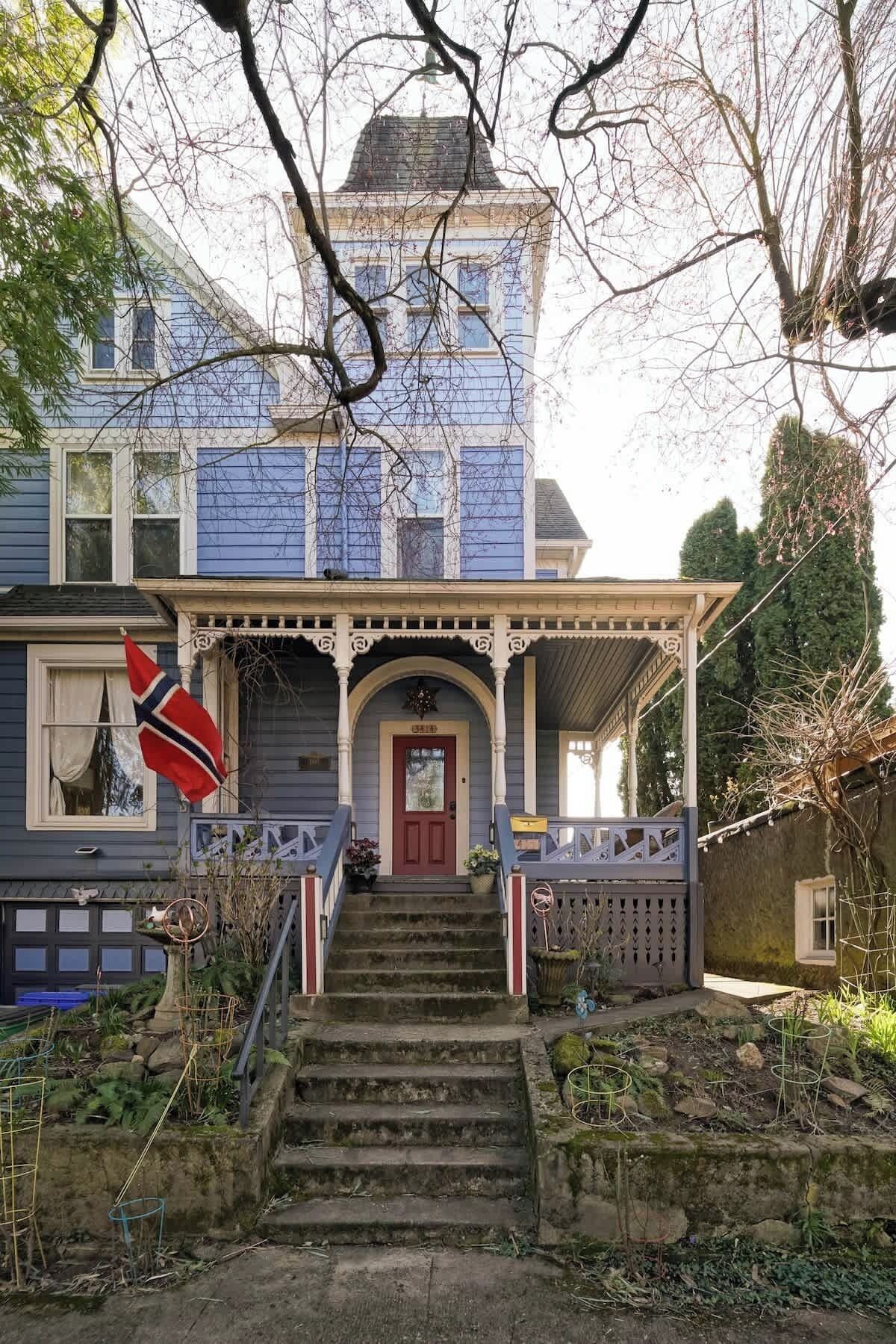 Une maison à deux étages avec un porche à l’avant, une porte rouge et un drapeau.