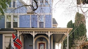 Une maison à deux étages avec un porche à l’avant, une porte rouge et un drapeau.