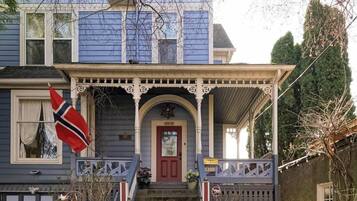 Une maison à deux étages avec un porche à l’avant, une porte rouge et un drapeau.