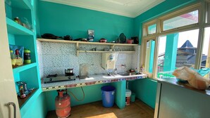 A kitchen with teal walls, a gas stove, a sink, and a window with a view of buildings outside. - Jagatram Niwas (Dharamshala)