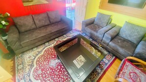 A living room with two sofas, a coffee table, and a TV mounted on the wall. - Jagatram Niwas (Dharamshala)