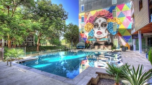 A swimming pool with a colorful mural on the adjacent building, surrounded by trees and potted plants.
