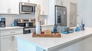 A modern kitchen with white cabinets, stainless steel appliances, and a wooden tray with a 'thank you' card.