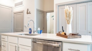 A modern kitchen with a stainless steel dishwasher, white cabinetry, and a countertop with a vase of pampas grass.