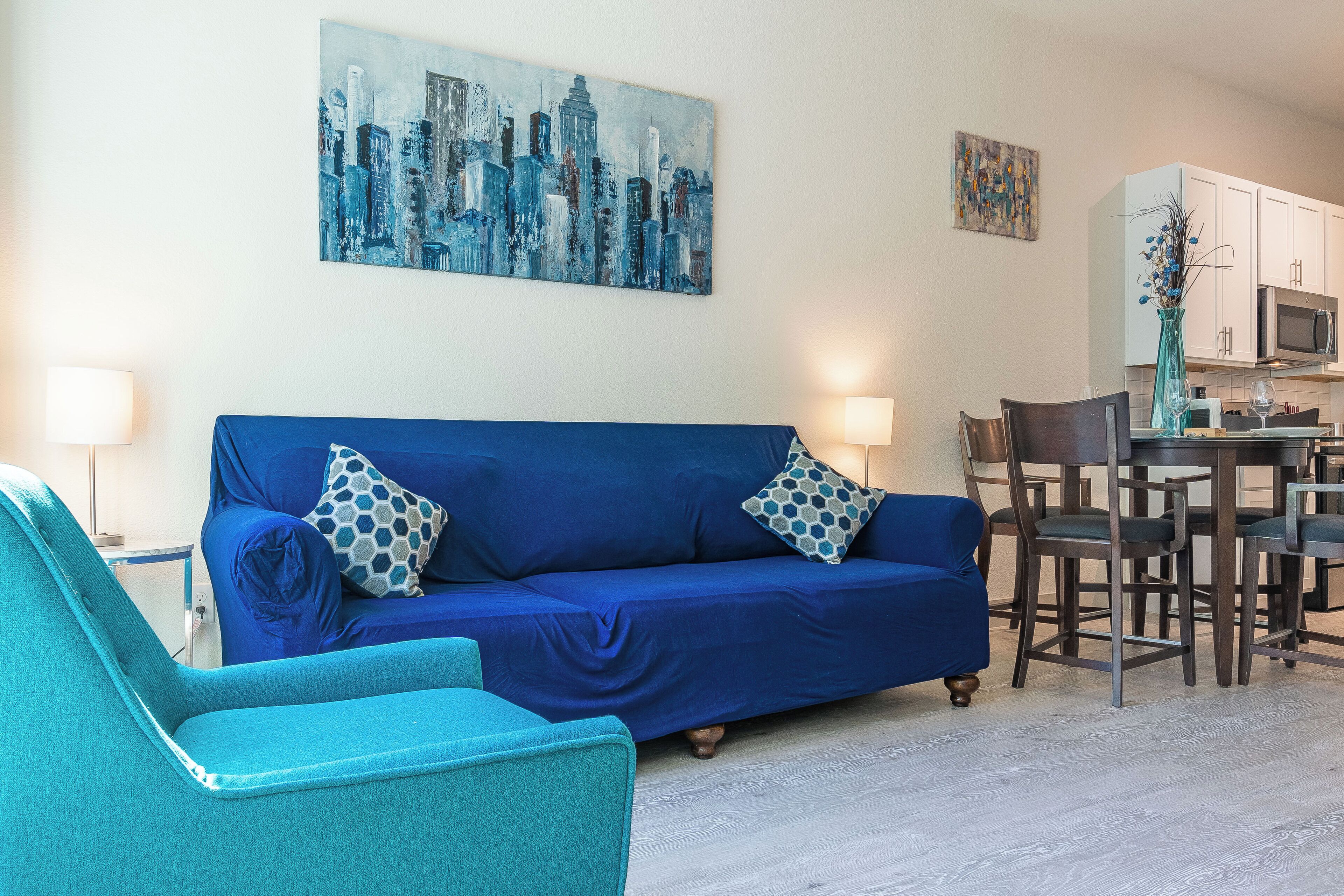 Una sala de estar con un sofá azul, un sillón turquesa y un comedor con mesa y sillas.