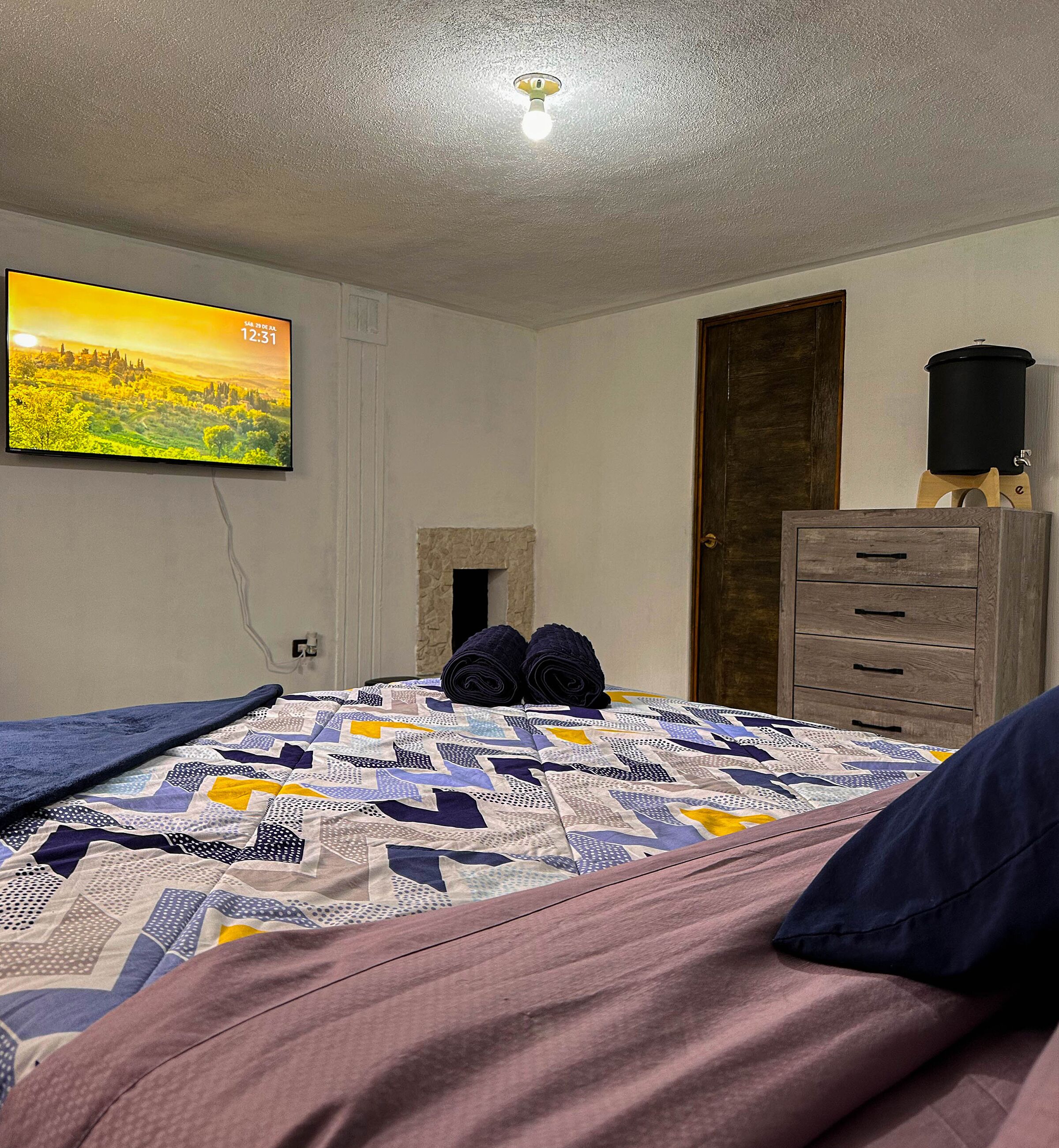 Une chambre à coucher avec un lit, un téléviseur diffusant un paysage, une cheminée et une commode en bois.