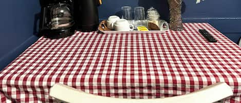 A checkered table with a coffee maker, cups, a tray, salt and pepper shakers, a vase with flowers, and a remote control.