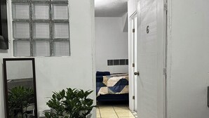 A hotel room with a bed, a potted plant, a tiled floor, and a door with a sign above it. - Hospedajes Alta Terra (Quetzaltenango)