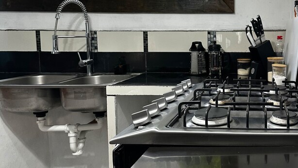 A modern kitchen with a gas stove, stainless steel sink, and a window overlooking a garden. - Hospedajes Alta Terra (Quetzaltenango)