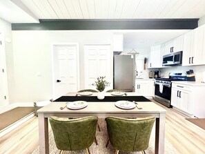 A modern kitchen with white cabinets, a stainless steel refrigerator, and a microwave. There is a dining table with chairs and a small potted plant. - Luxury•PickleBall•Golf•Pool•HotTub•Grill•Arcades•6 TV’s•Playground• .5 Acre (El Cajon)