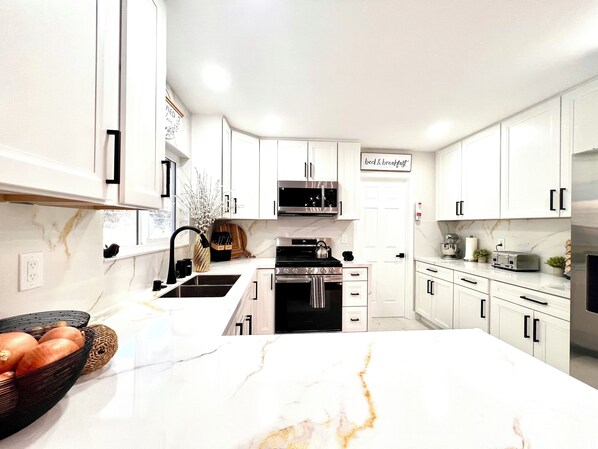 A modern kitchen with white cabinets, a marble countertop, and stainless steel appliances.