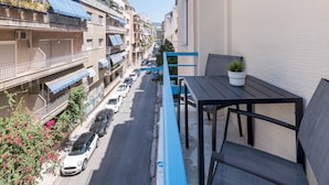 A balcony with a table and chairs, overlooking a street with parked cars and buildings. - Lycabettus Modern Retreat (Athina)