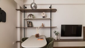 A modern dining area with a white table, two green chairs, a pendant light, and a TV on a wooden shelf. - Lycabettus Modern Retreat (Athina)