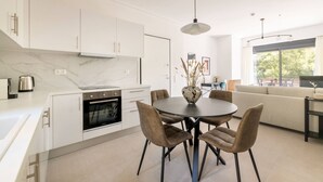 Une cuisine moderne avec des meubles blancs, un four encastré et un coin repas comprenant une table ronde et des chaises.