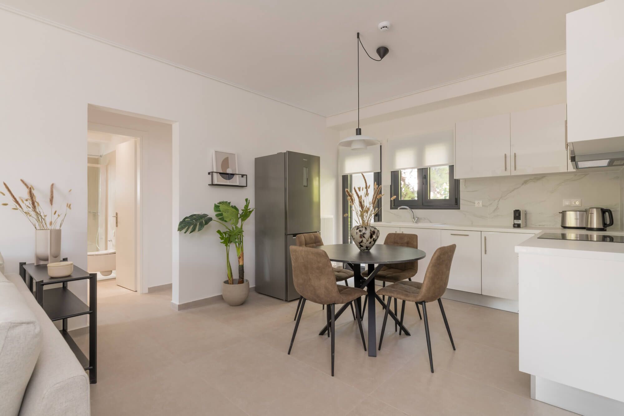A modern kitchen with white cabinets, a dining area with a round table and chairs, and a visible refrigerator.