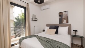Une chambre d’hôtel moderne avec un grand lit, une vue sur l’extérieur grâce à une porte coulissante, un ventilateur de plafond et un tableau abstrait encadré.