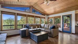 A spacious living room with a large sofa, a coffee table, and a view of the outdoors through large windows. - Xbox*Ping Pong* Pop-a-shot*Game Room* (Flagstaff)