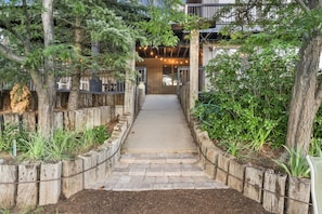 A pathway leading to a building with a covered entrance, surrounded by trees and wooden fences.