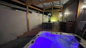 Ein Whirlpool mit blauem Licht, Holzbalken, einer kleinen Insel mit Pflanze und einem gefliesten Boden.