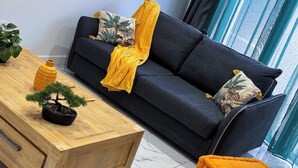 Ein modernes Wohnzimmer mit einem dunkelgrauen Sofa, einem Holztisch und einer kleinen Topfpflanze.