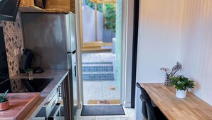 Eine moderne Küche mit einer Holzausziehtafel, einem eingebauten Backofen und einer Mikrowelle. Auf der Arbeitsplatte steht eine kleine Pflanze und am Esstisch ein schwarzer Stuhl.