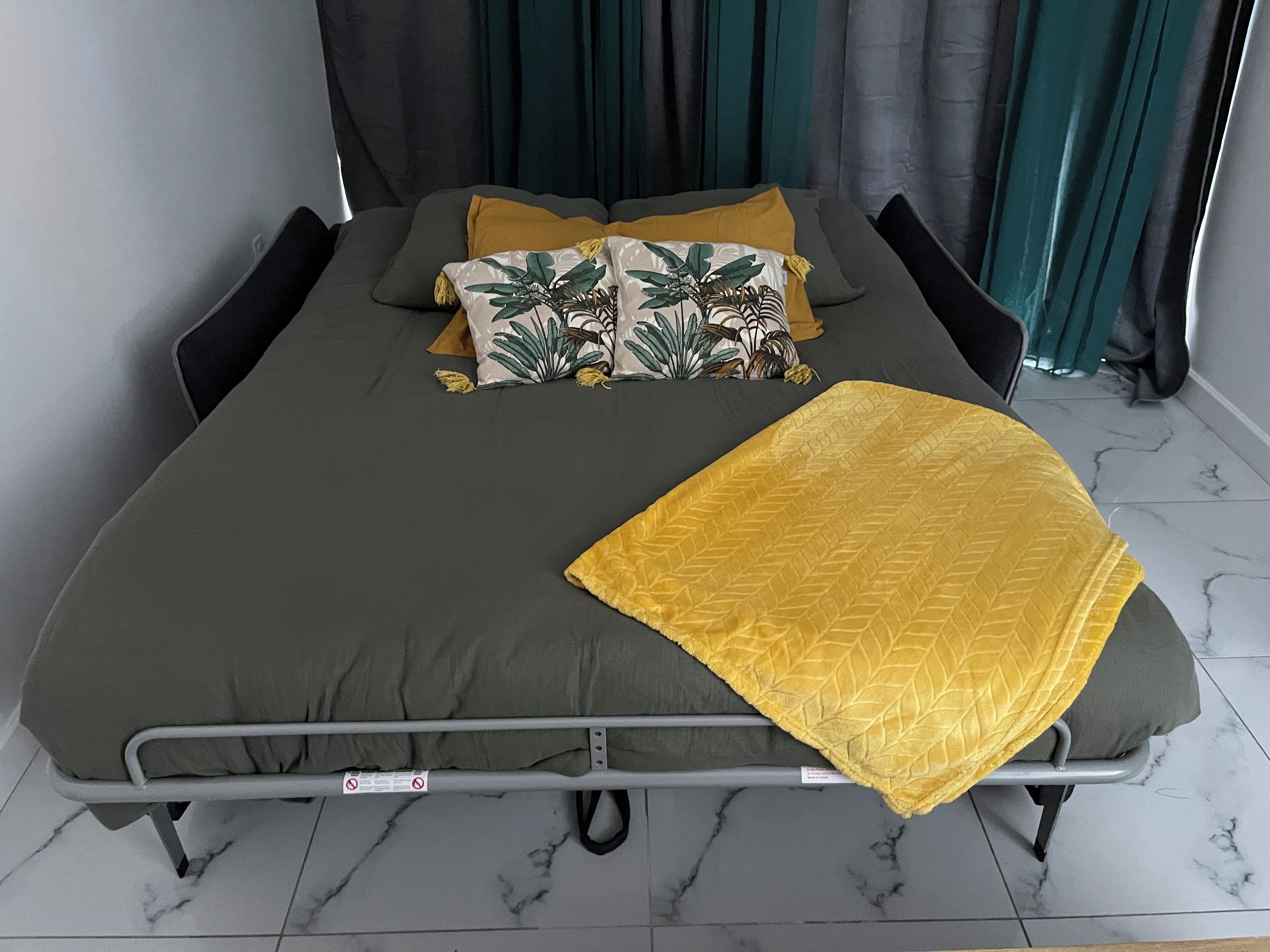A bed with a metal frame, grey bedding, and a yellow throw blanket.