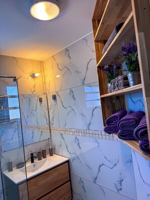 A bathroom with marble walls, a wooden vanity, a sink, and shelves with towels and plants. - Villas Sauvages, Manapany-les-bains. (Saint-Joseph)