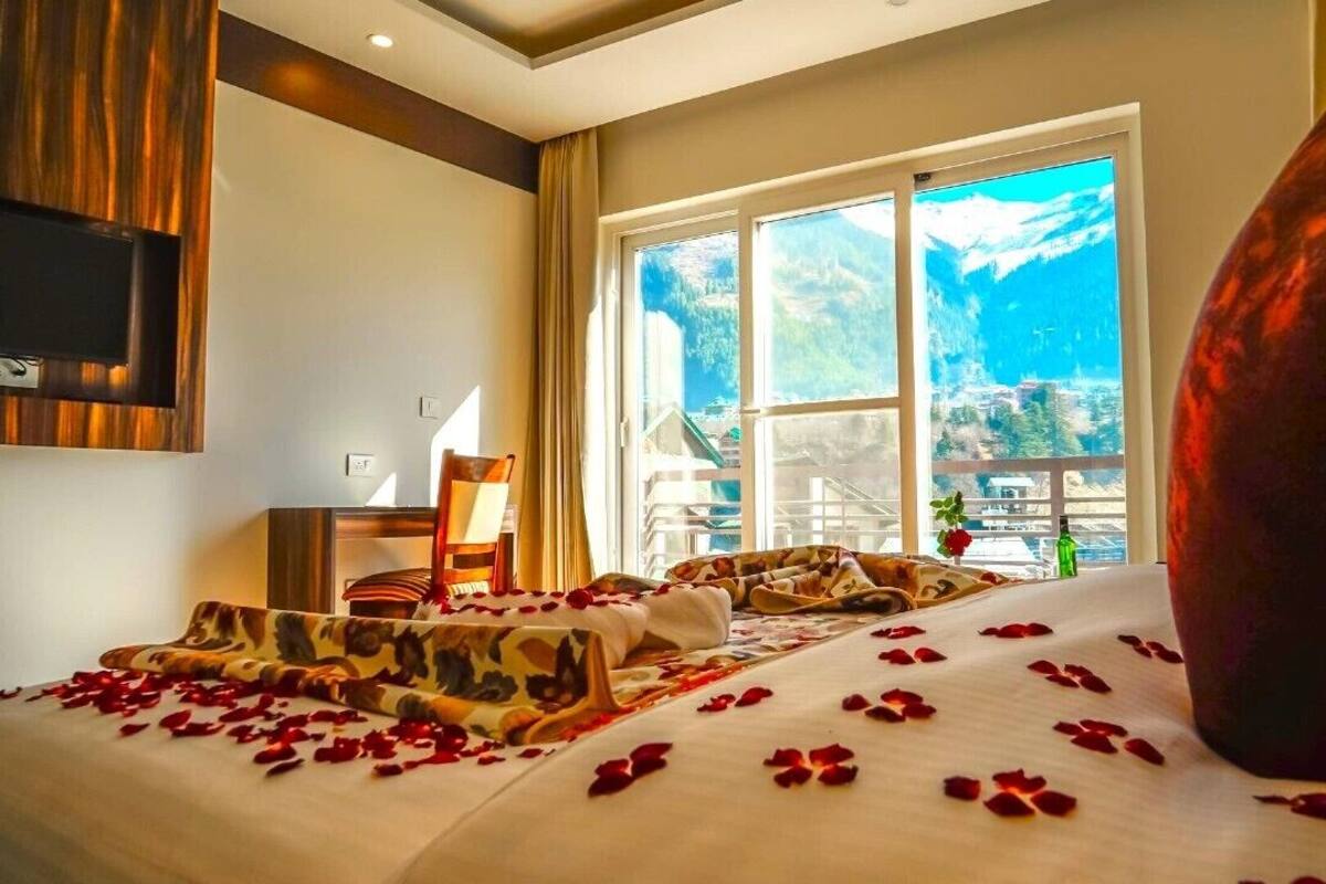 A hotel room with a bed, a large window, and a view of mountains.