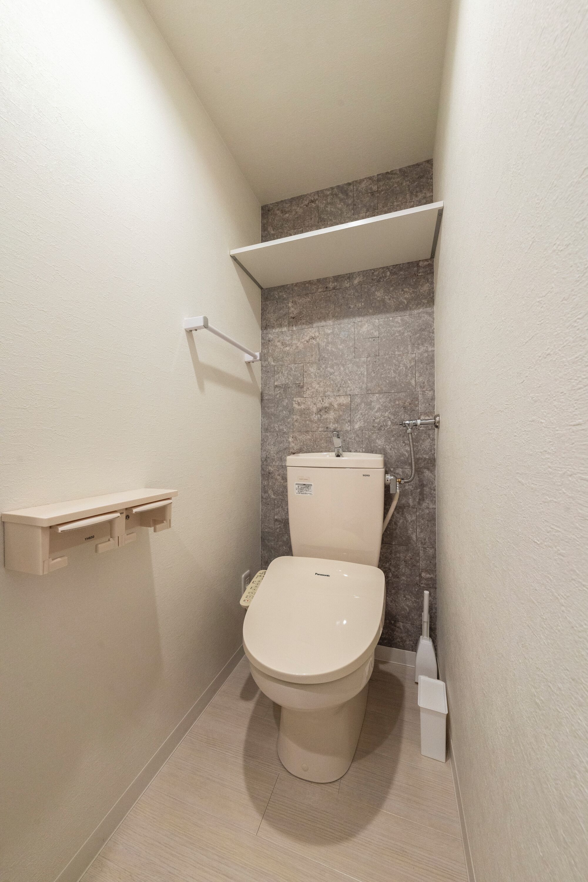 A small, modern bathroom with a toilet, a shelf above the toilet, and a showerhead.