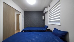 A bedroom with two beds, a wooden door, a wall-mounted air conditioner, and a window with blinds. - Apollo (Hakodate)
