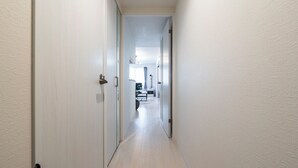 A narrow, light-colored hallway with white walls and a wooden floor. - Apollo (Hakodate)