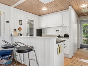 A modern kitchen with white cabinetry, a built-in oven, and a bar area with stools.