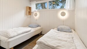 Une chambre avec deux lits simples, une étagère en bois et deux lampes fixées au mur.