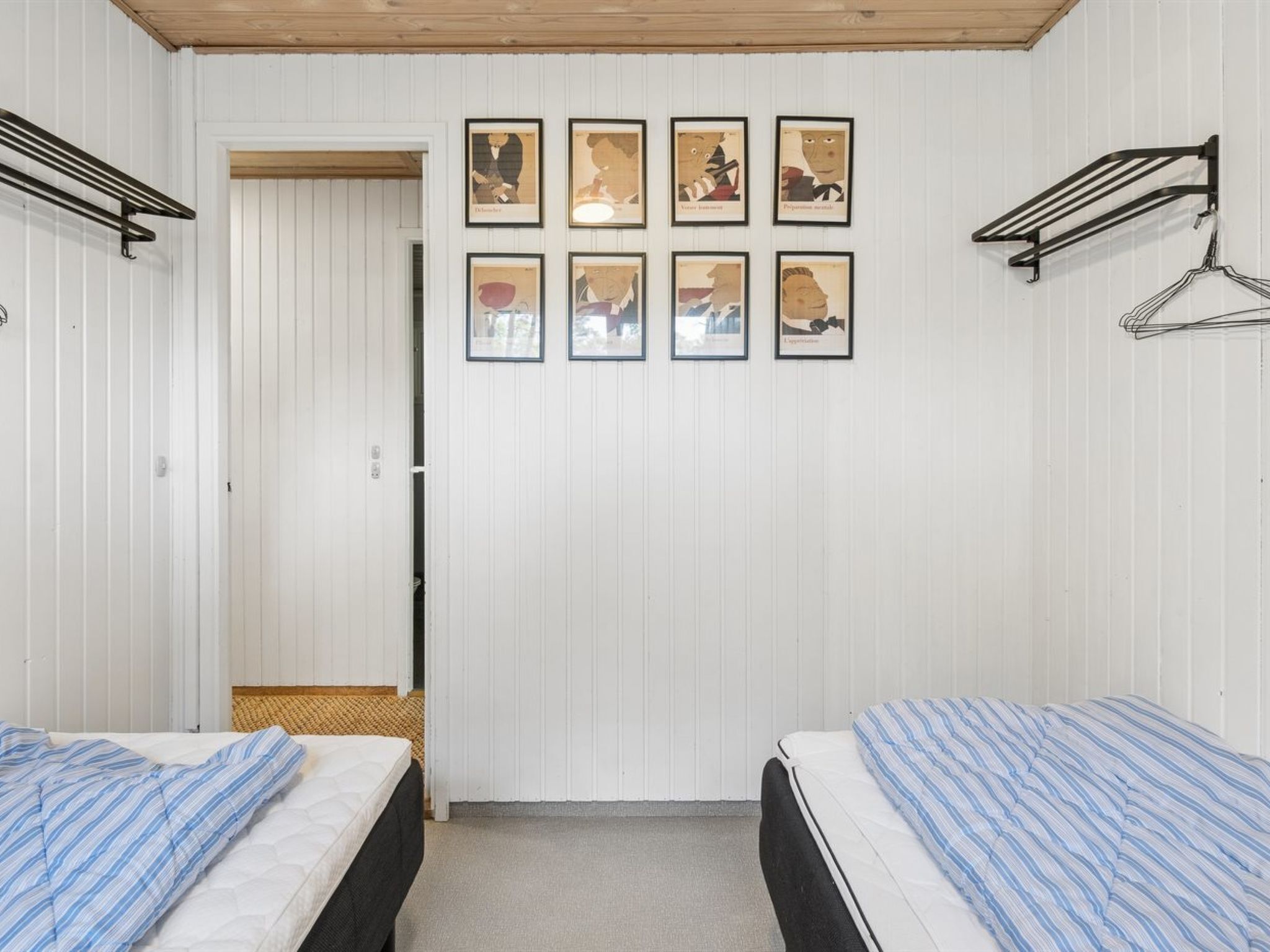 Habitació amb dos llits, una porta i una paret amb quadres emmarcats.