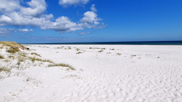 Une vaste plage de sable, bordée de dunes, et un ciel bleu azur.