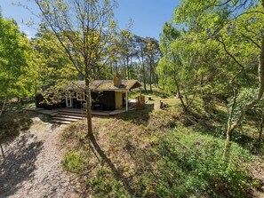 A cabin with a deck, surrounded by trees and a gravel path.