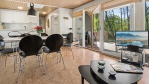 Une cuisine moderne avec des meubles blancs, un coin repas avec des chaises noires et un grand téléviseur posé sur un meuble.