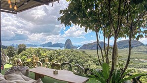 Una terrazza con vista su un paesaggio montuoso, un tavolo e diverse zone relax con cuscini.