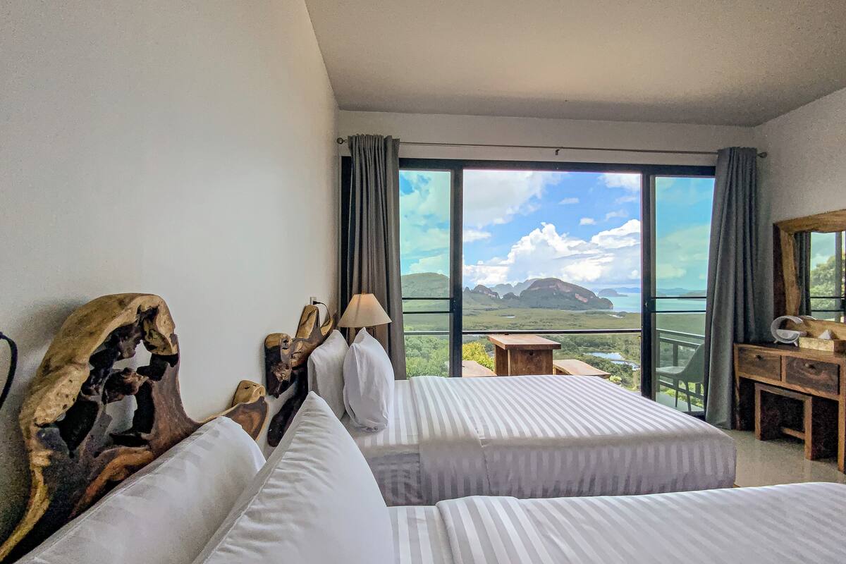 A hotel room with two beds, a wooden headboard, a desk, and a view of the landscape.